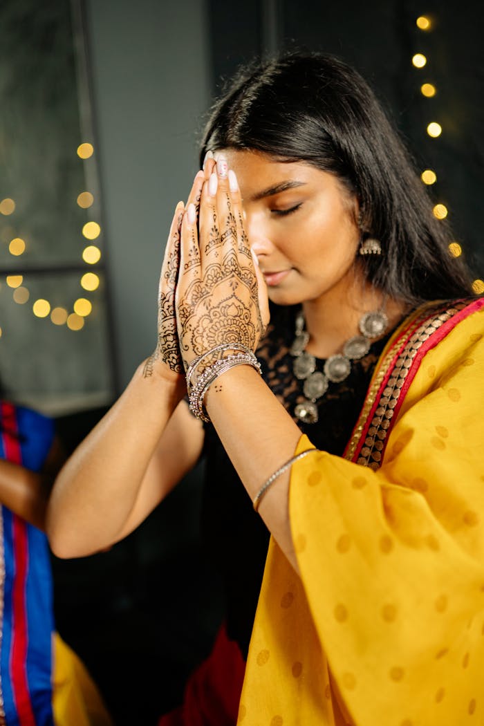 South Asian woman praying with henna designs during a festive Diwali celebration.